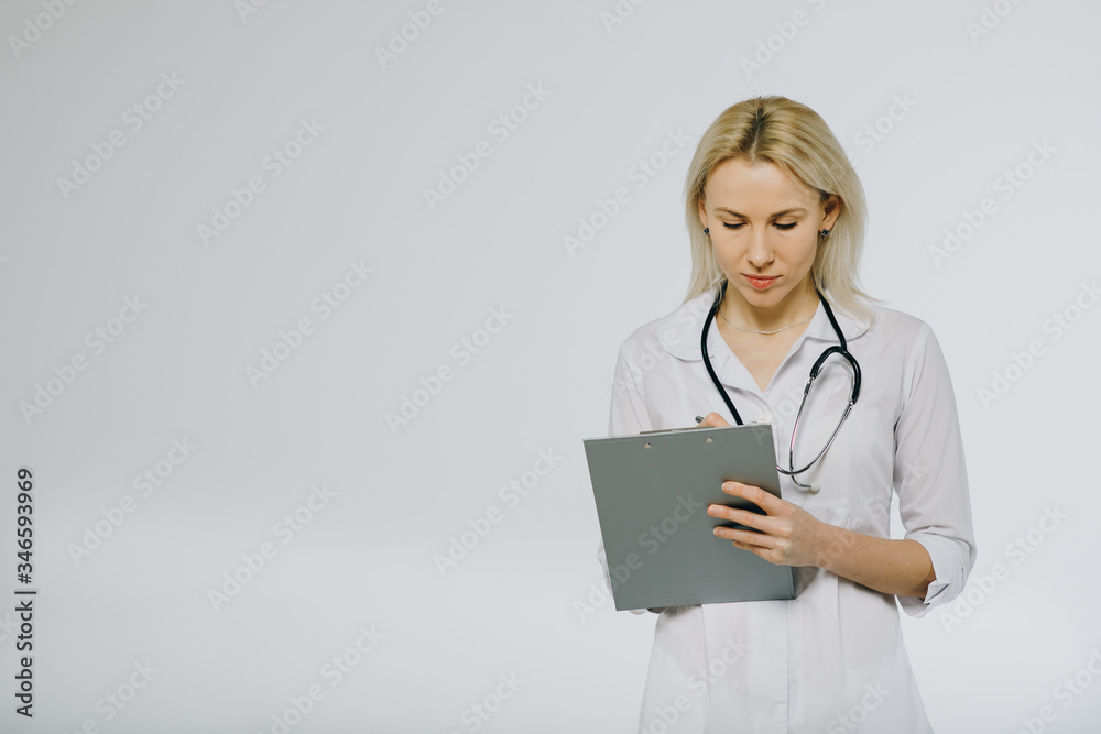 Beautiful confident female doctor in white medical coat and stethoscope looking calm on clipboard with patients medical history. Copy space. Clinic ads and offers. Beautiful confident female doctor in white medical coat and stethoscope looking calm on clipboard with patients medical history. Copy space. Clinic ads and offers.