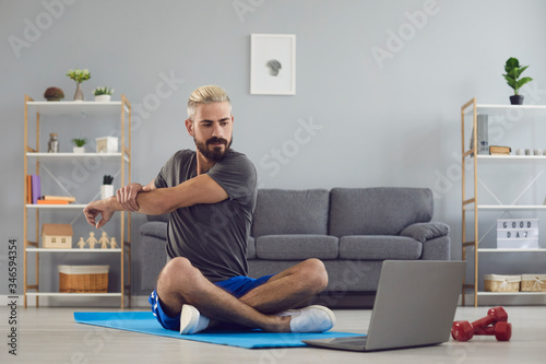 Workout exercise fitness online video call. Man doing warm up stretching exercises online fitness in a laptop video chat at home.