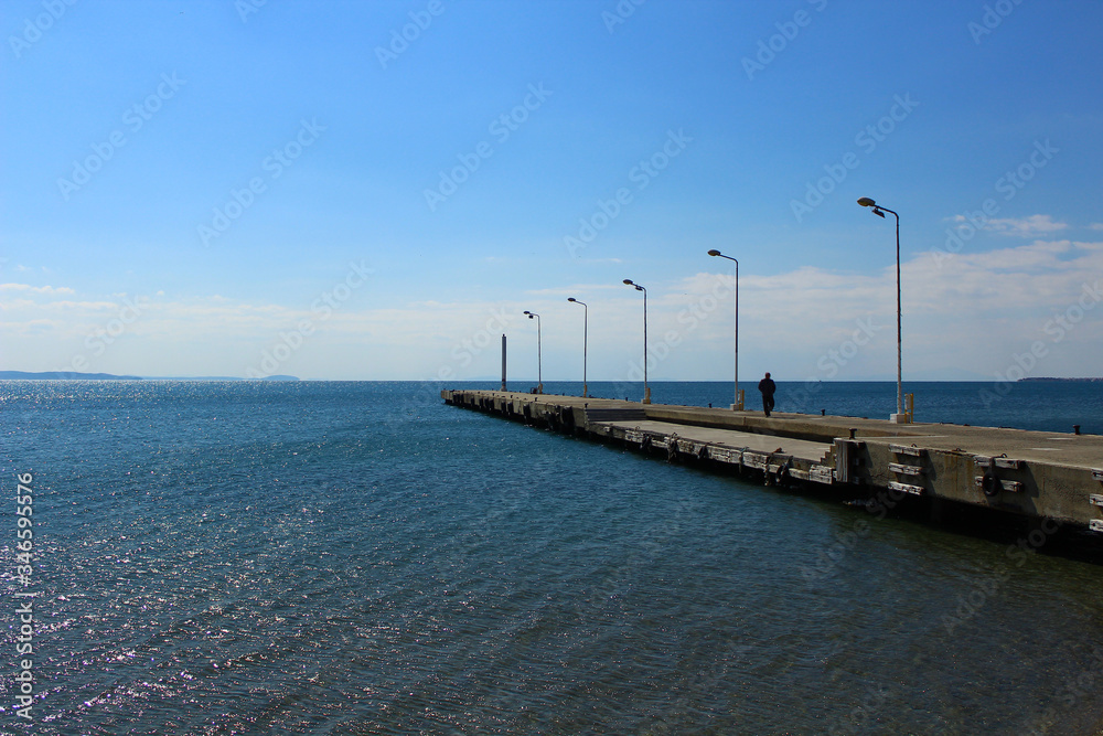 Seaside and concrete pier. A man walking on the pier. Photo was taken in sunny outdoors.