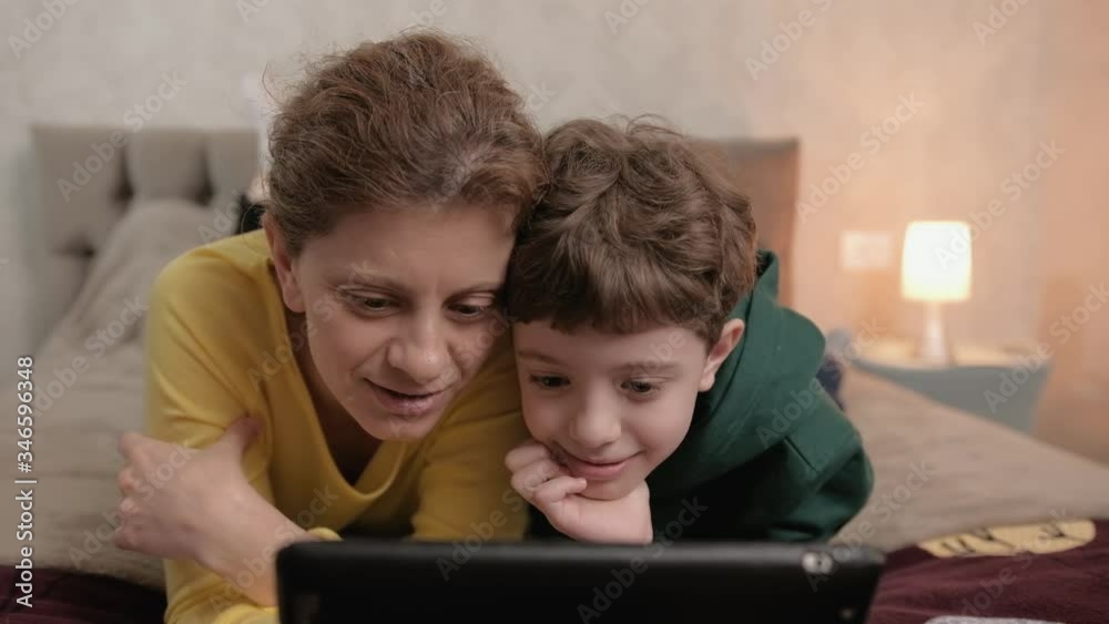 Mom and son watching educational video on the tablet. Lying on the bed Mom and son watching educational video on the tablet. Lying on the bed