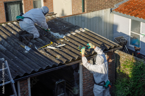 Professional asbestos removal. Man in protective suite removes asbestos roofing. photo