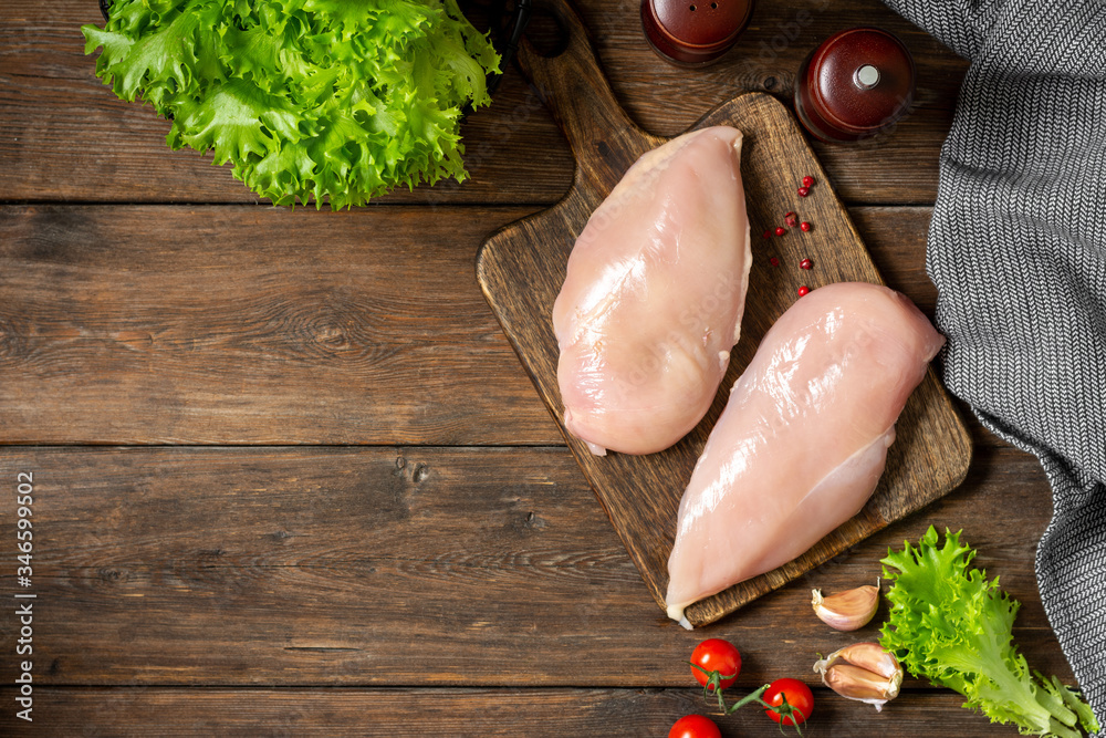 Chicken breast fillet on a wooden Board on a brown wooden table. Raw chicken breast. Top view with space for text