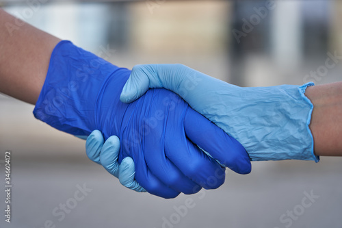 Human hands in protective gloves against covid-19 coronavirus pandemic, handshake in quarantine outdoors in city