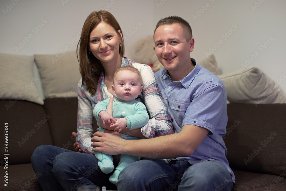 Young couple sitting on couch with his 3 months old baby boy, posing for family photo