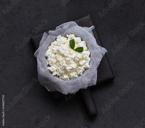 Cottage cheese on cheesecloth in a bowl on a wooden Board on a dark background in rustic style top view photo