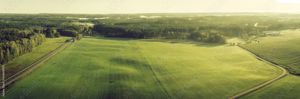 Warm aerial panorama view of picturesque autumn morning sunrise. Diagonal forest, road, crop field mist and power lines.