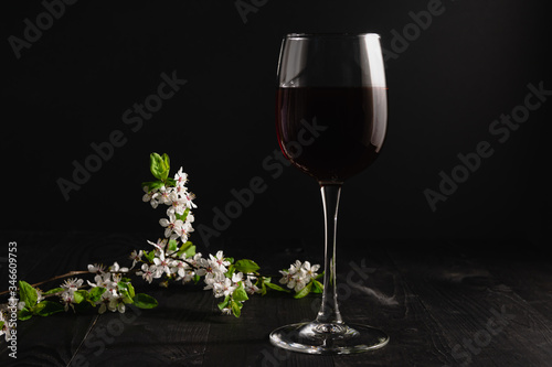 Glass of red wine and flowering apricot branch on a dark background. Alcoholic drink with fruity notes.