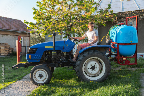 Young man farmer in white t-shirt driving blue tractor with sprayer