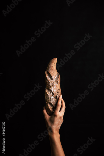 A woman hand holding a handmade rye bread from the bottom on a black background.