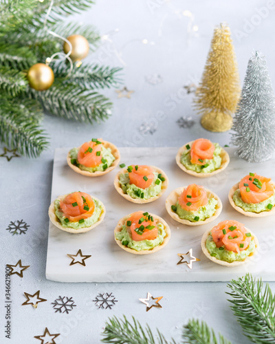 Holiday appetizer canapes with salmon avocado cream cheese on a light background with Christmas decorations. Festive table recipe ideas for New Year's and Christmas holidays.