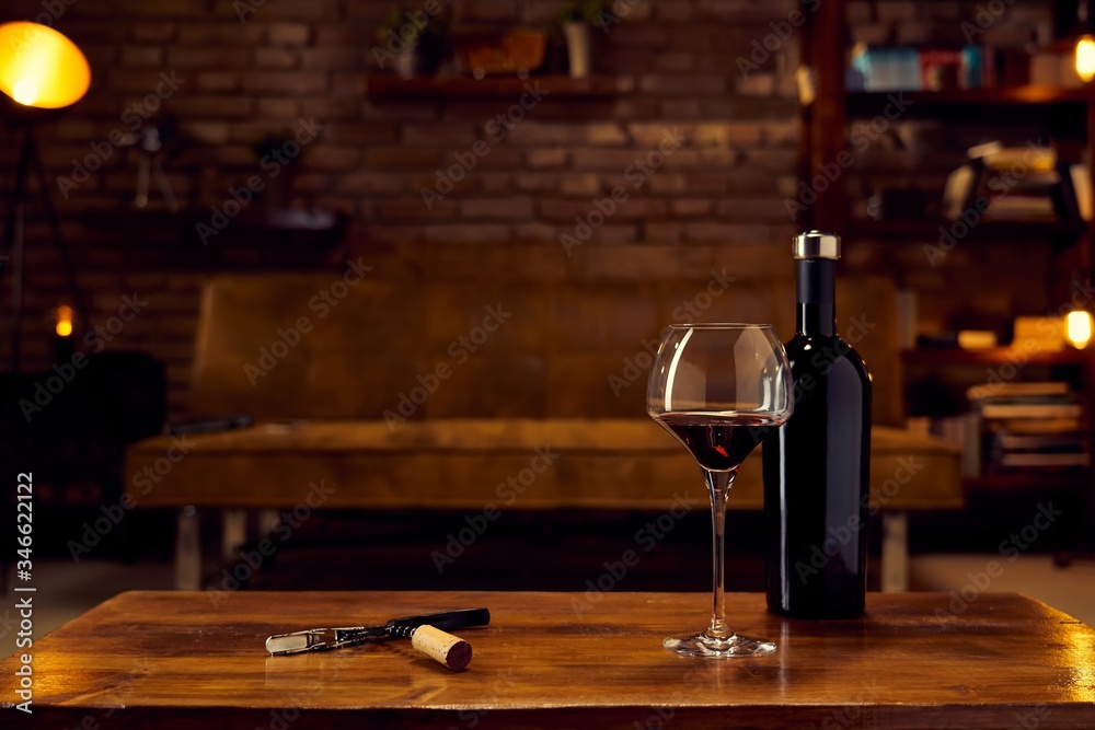 Wine glass and a bottle of red wine on table at home, cosy dark living