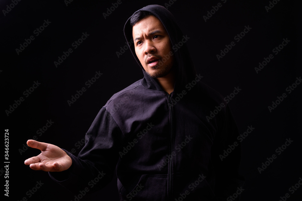 Portrait of stressed young Asian man in hoodie complaining with hand raised Portrait of stressed young Asian man in hoodie complaining with hand raised