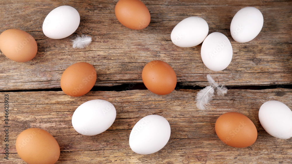 A few of white and brown chicken eggs and small feathers near with it on an old wooden table. A few of white and brown chicken eggs and small feathers near with it on an old wooden table.