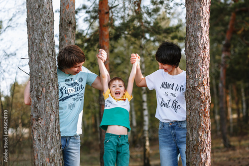 Parents hold their son's hands up as they stand between the pines