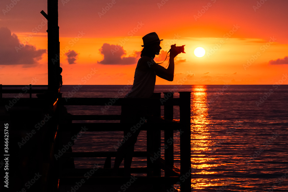 Fototapeta premium A silhouette of a girl photographer with a camera on the pier. Beautiful sunset.