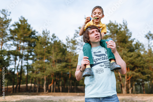 A son sitting on his father's neck. Family inflates soap balloons
