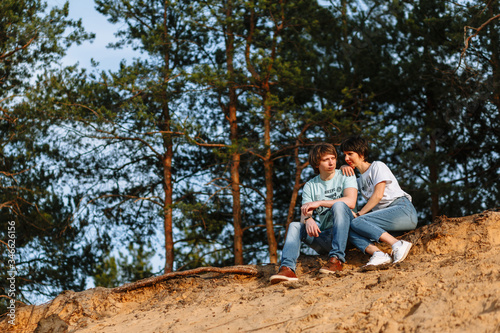 Lovers sit on a sandy cliff against the background of a forest
