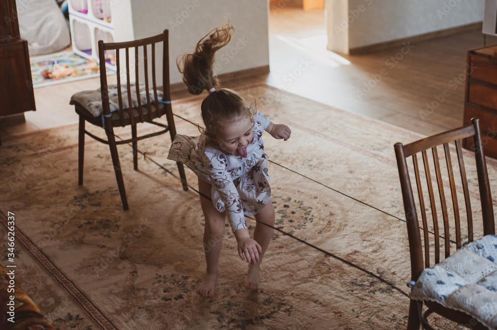 Naklejka premium A happy girl jumps through an elastic band strung between chairs. Idea for quarantined child activity