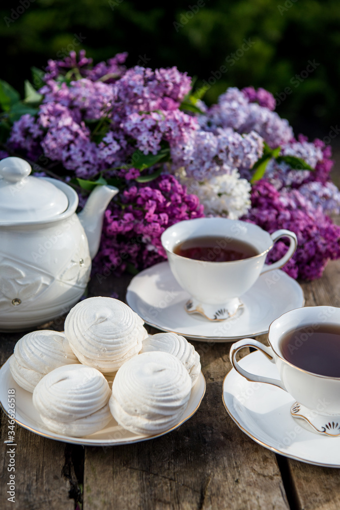 Lilac spring flowers in vase on wooden background. Tea coffee cup on table during breakfast time Lilac spring flowers in vase on wooden background. Tea coffee cup on table during breakfast time