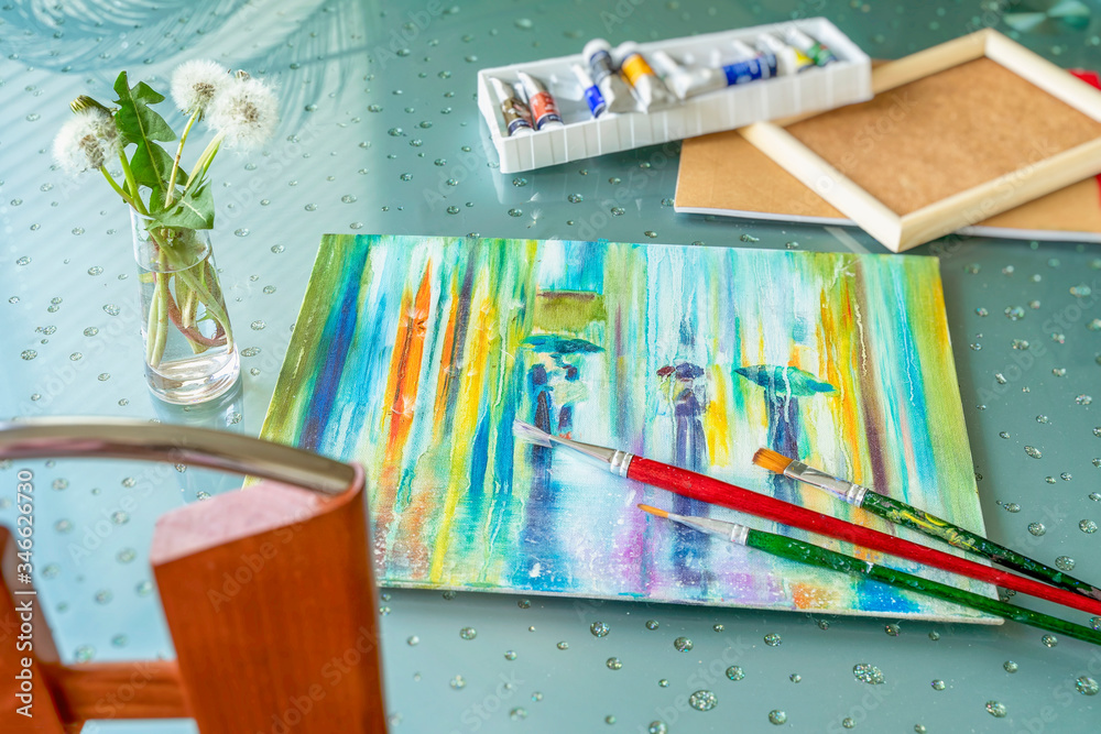 Table with a lying oil painting on canvas, box of paints in tubes, brushes and bouquet of fluffy dandelions. Romantic concept of spring, leisure, hobbies.