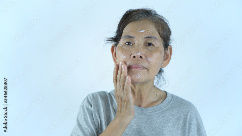 Beauty concept. An old woman applying cream on a white background. 4k Resolution.