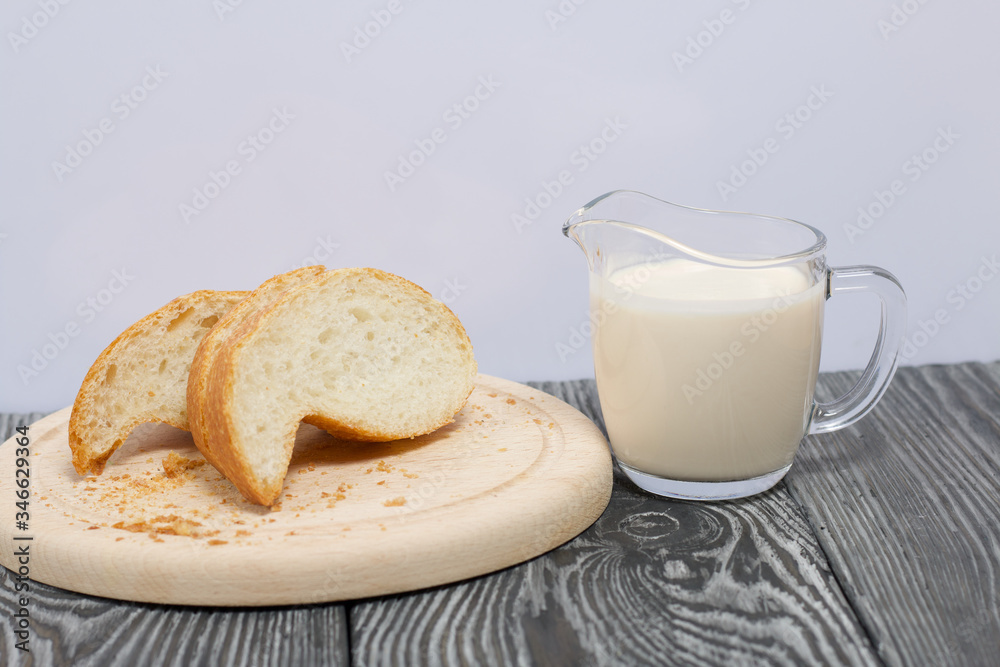 A glass of fermented baked milk and slices of ciabatta bread on a cutting board. On brushed pine boards. A glass of fermented baked milk and slices of ciabatta bread on a cutting board. On brushed pine boards.