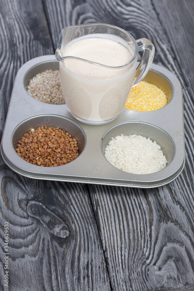Glass with milk. Nearby in the container are cereals: buckwheat, rice, and barley corn. On brushed pine boards. Glass with milk. Nearby in the container are cereals: buckwheat, rice, and barley corn. On brushed pine boards.