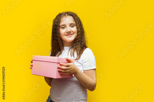 Little cute girl holding gift box on Yellow background.
