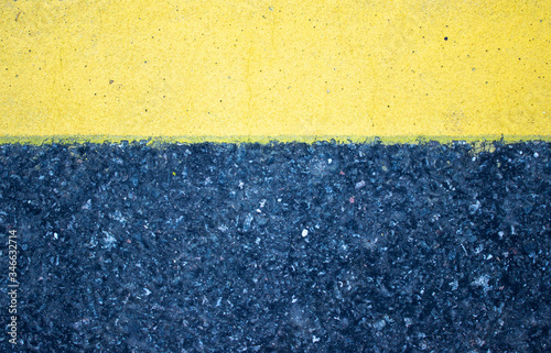 A rough look of asphalt with a pronounced yellow stripe horizontally from above. photo