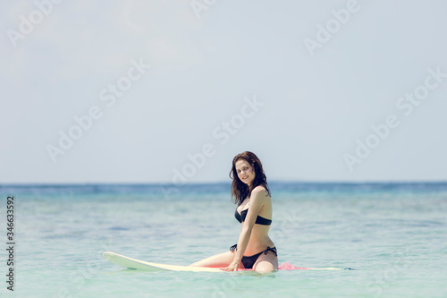 Beautiful surfing girl in bikini and with wet hairs sitting on a front of big longboard surf board and waiting for the wave in open ocean water. Modern active sport lifestyle and summer vacation. © Whiteline