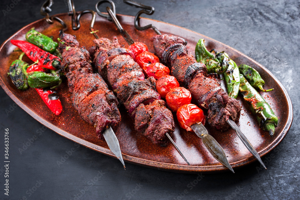Traditional Russian shashlik on a barbecue skewer with vegetable and sumach as top view on a wooden cutting board
