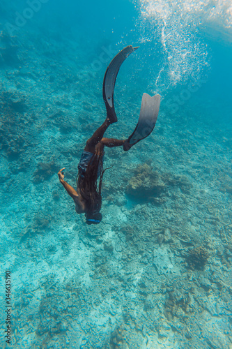 Man freediver with dreads diving down into the deep blue water of the tropical ocean. Freediving lifestyle and extreme water sport adventure concept.
