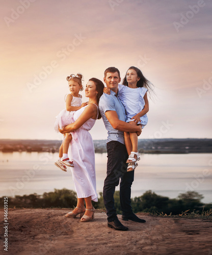 happy family of father, mother and two daughters on a hill at sunset