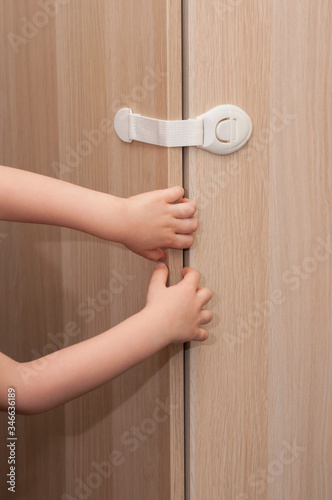 Hands of a little kid pulling the closet door closed with a special lock for child safety