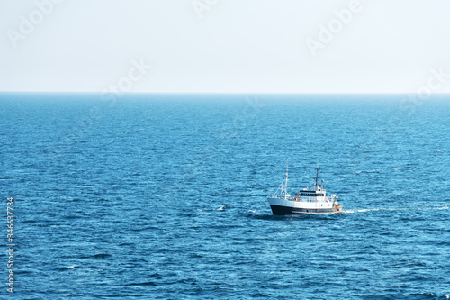 Lonely fishing ship trawler boat on ocean water. Calm clear sea sunny weather. Beautiful horizon of seascape