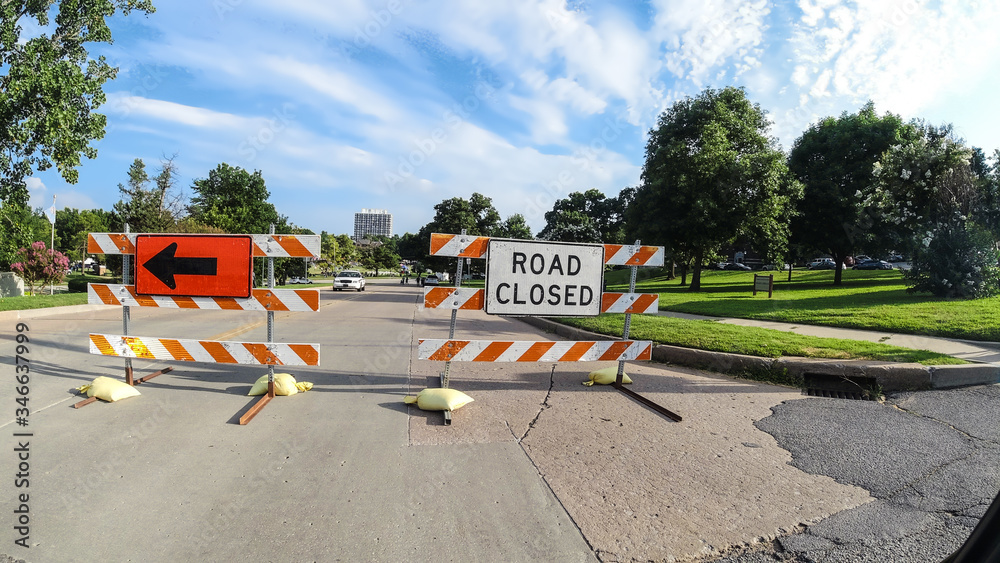 Road Closing and Detour signs blocking road during an event with Police cars and people walking in the distance in summer under pretty sky Road Closing and Detour signs blocking road during an event with Police cars and people walking in the distance in summer under pretty sky