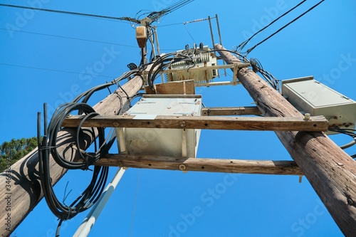 Electric transformer on wooden poles, blue sky background