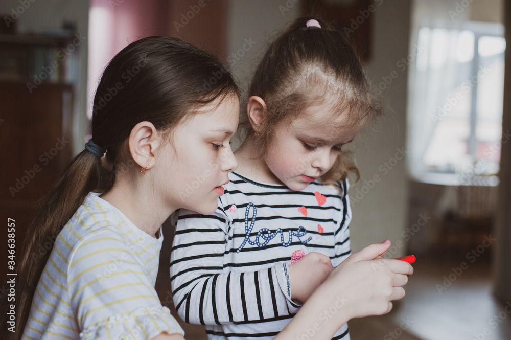Happy little girls with a smartphone in hands communicate at home with loved ones using modern technology Happy little girls with a smartphone in hands communicate at home with loved ones using modern technology