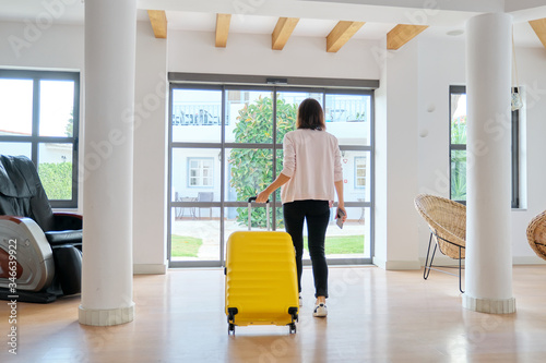 Woman tourist guest with suitcase in hotel lobby, back view
