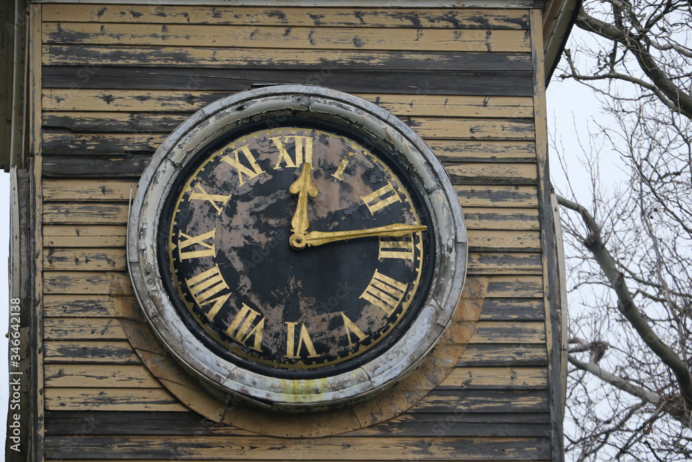 Close-up of a round clock face in a wooden tower with peeling paint and gold coloured clock hands and roman numerals in Kent, England, UK.