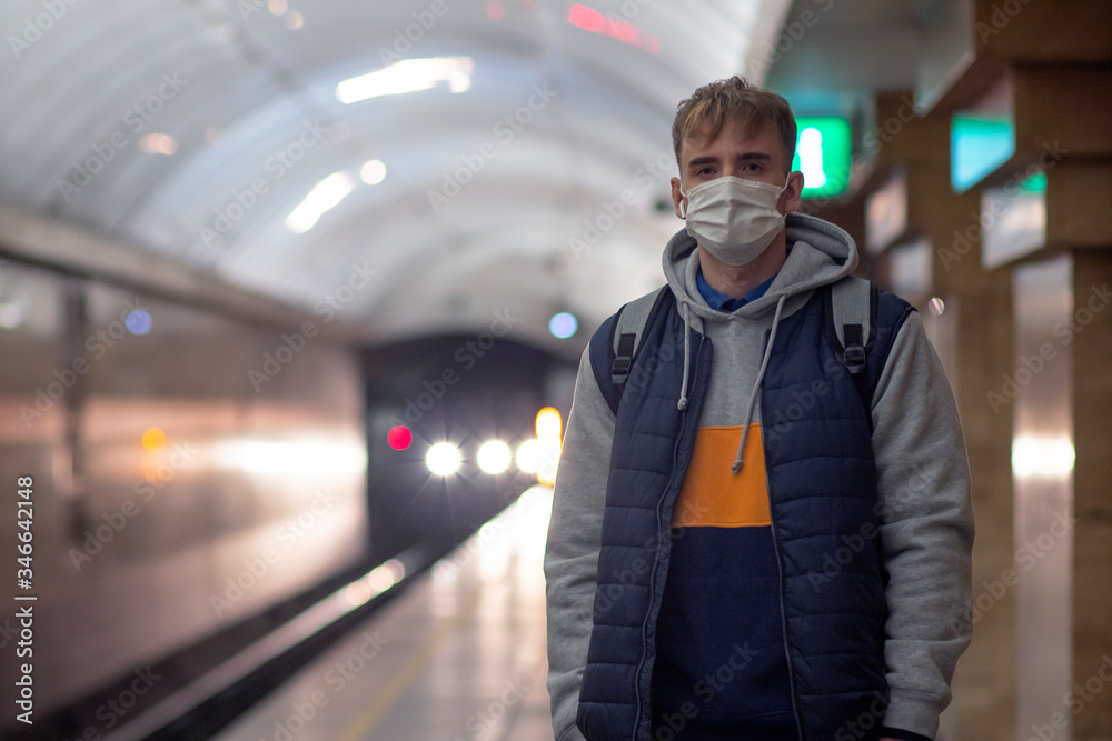 Young guy man, in a protective medical mask, against the background of the subway, tunnel, Waiting for a train. Epidemic concept, pandemic virus