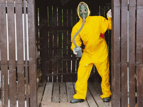 human in a gas mask and protective yellow costume peeps out of the doorway photo