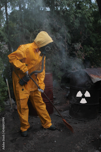 human in a gas mask and a protective yellow suit works against a smoking barrel with a radiation hazard sign