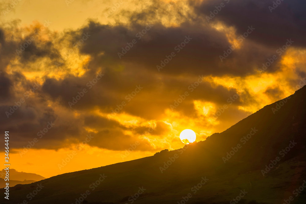 Sun setting at Sunset behind Mountainside, Clouds 