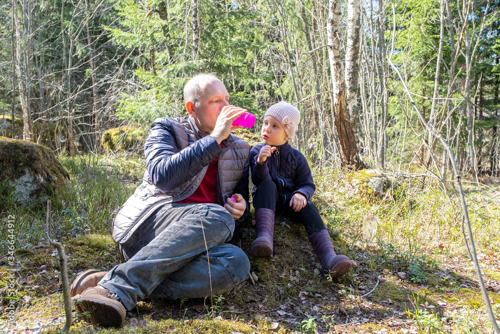 Walk in the forest, dad and daughter relax and drink water while admiring nature.
