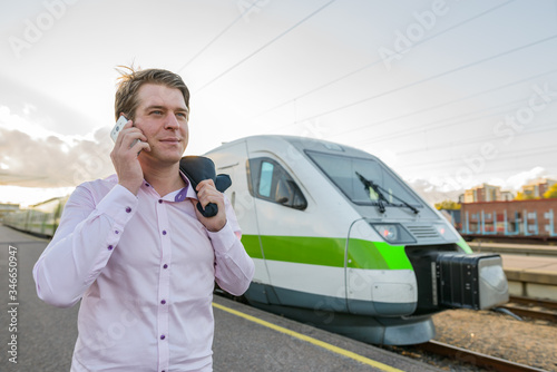 Young handsome businessman talking on mobile phone in front of train at railway station