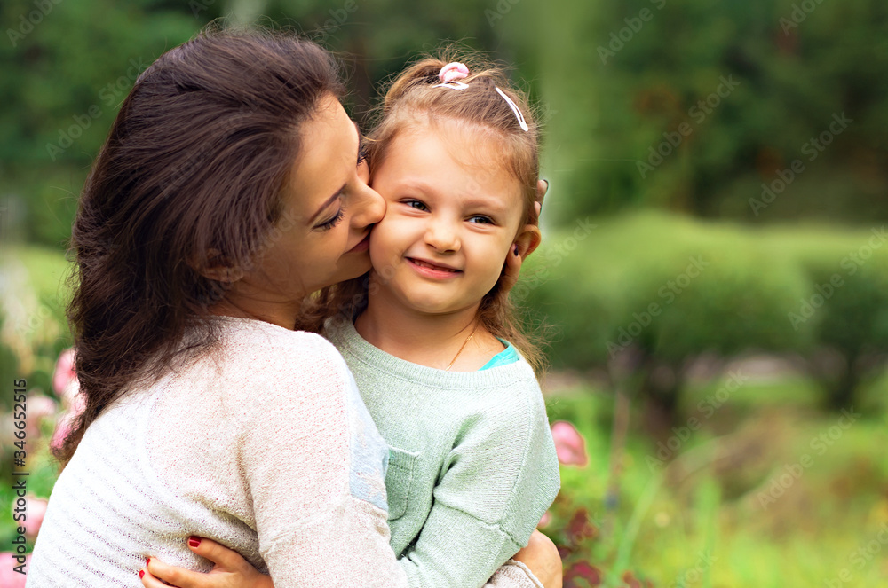 Beautiful mother and cute small daughter kissing on summer green background. Closeup Beautiful mother and cute small daughter kissing on summer green background. Closeup