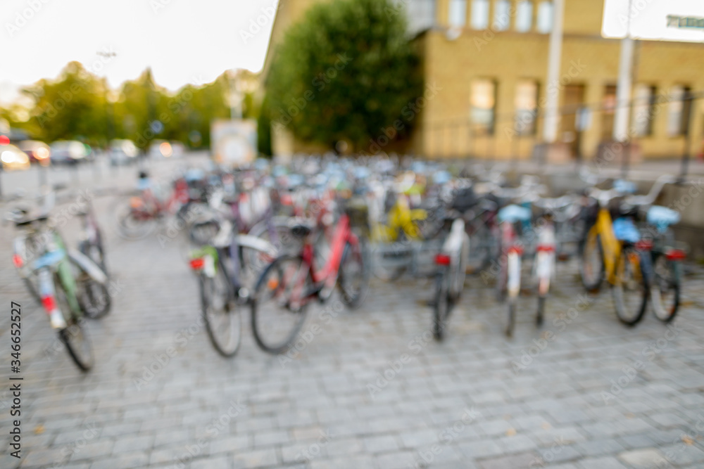 Defocused row of bicycles parking in squarestreet near fenced court and building