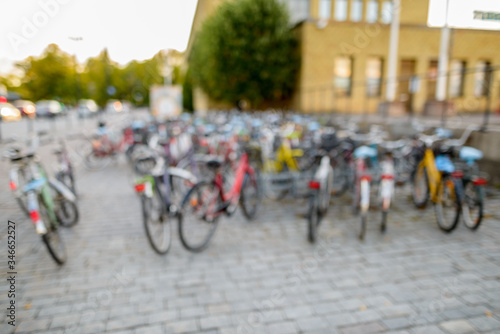 Defocused row of bicycles parking in squarestreet near fenced court and building