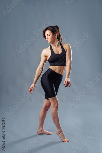 Pretty Hispanic personal trainer and diet coach standing isolated on gray background. Health and fitness concept - portrait of an caucasian american girl posing with fitness clothes. Hugging herself